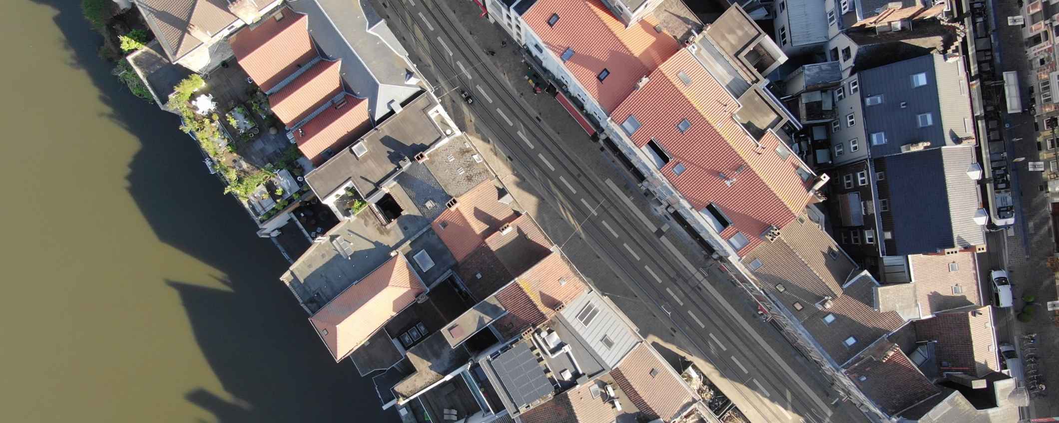 Luchtfoto van een straat langs het water met dicht op elkaar gebouwde huizen. Op de daken liggen zonnepanelen en lopen tramsporen door de straat.